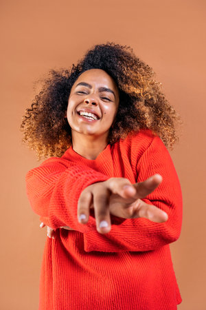 Beautiful black woman with curly hair having fun and looking at camera in studio shot against brown background.の写真素材