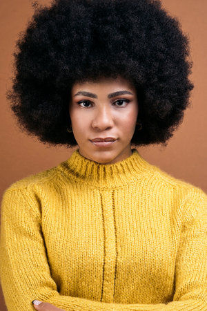 Beautiful young afro woman posing in studio shot against brown background and looking at camera.の写真素材