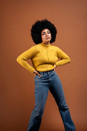 Beautiful young afro woman posing in studio shot against brown background and looking at camera.