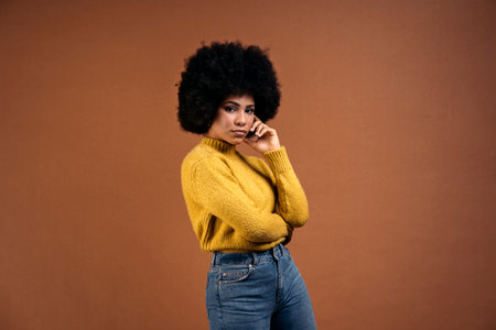 Beautiful young afro woman posing in studio shot against brown background and looking at camera.の写真素材