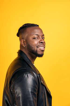 Confident black man wearing black leather jacket smiling and looking at camera in studio shot.の写真素材