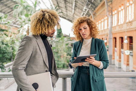 Business woman wearing formal clothes talking with her colleague and using digital tablet in a train station.の写真素材