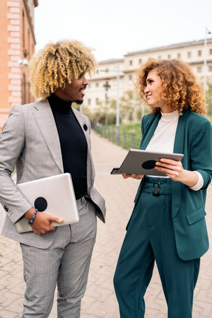 Happy afro business man wearing formal clothes talking with his coworker and holding laptop in the street.の写真素材