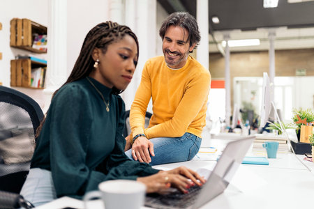 Adult business man working with his african coworker and smiling. They are using a laptop.