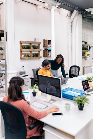 Diverse office workers sitting in a big desk and working with laptops. Coworking concept.の写真素材