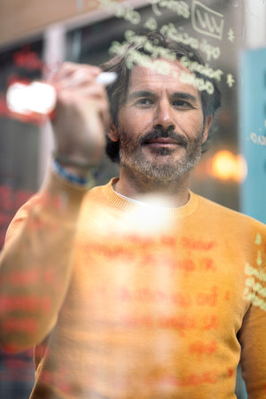 Bearded male office worker writing in white board and smiling. Co-working concept