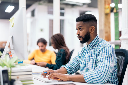 Afro american office worker sitting in his desk and using his laptop. He is concentrated and looking...