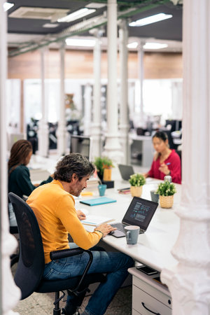 Multicultural teamwork sitting in big desk and using laptops in a modern bright office. Co-working conceptの写真素材