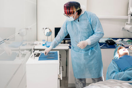 Dentist working in modern dental clinic and wearing face mask. He is also wearing protective...