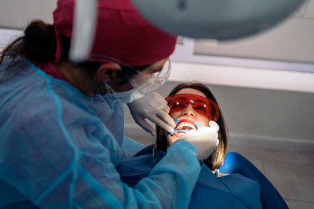 Female patient during check up in dental clinic. The dentist is wearing face mask and protective glasses.の写真素材