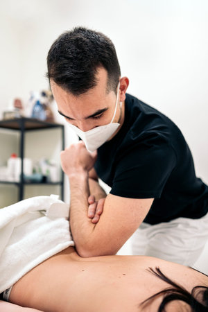 Professional worker in physiotherapy clinic wearing face mask working with unrecognized client.の写真素材
