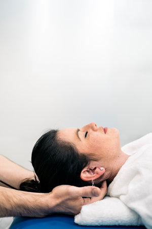 Relaxed woman enjoying neck massage while lying in stretcher.の写真素材