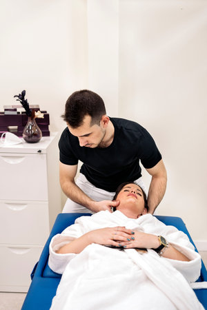 Male physiotherapist giving neck massage to relaxed woman lying in stretcher.の写真素材