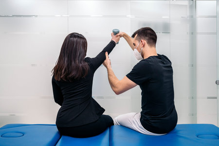 Male physiotherapist wearing face mask working with unrecognized patient in rehabilitation session.