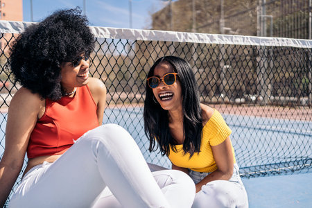 Pretty african american young women laughing and having fun while sitting in sports court.の写真素材