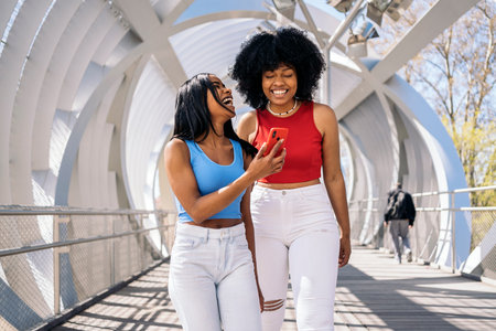 Happy black female friends laughing and using mobile phone in the city. One of them has cool afro hair.の写真素材