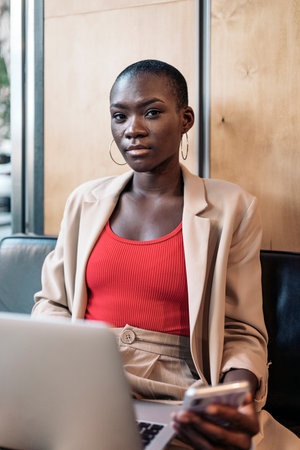 Portrait of an african american young adult woman with short hair sitting in a coffee shop using her laptop looking at camera.の写真素材