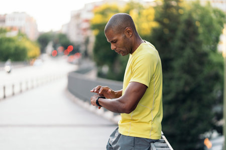 Side view of an African American man with yellow t-shirt using smartwatch to do sports in the city.