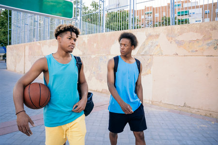 Two young athletic afro american men going to the basketball court holding bags and a basketball ball.の写真素材