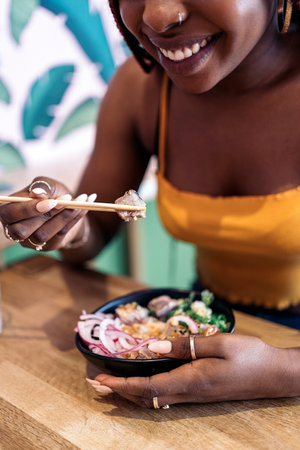 Unrecognized african woman sitting in a restaurant enjoying a healthy poke bowl.の写真素材