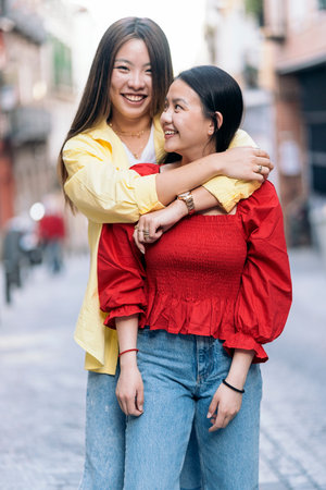Young asian woman having fun in the city of Madrid hugging her friend and looking at camera.