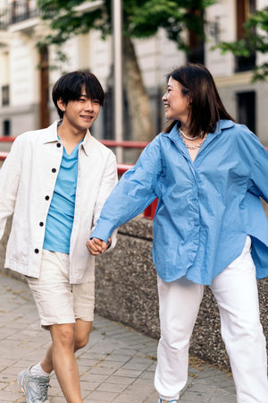 Happy asian couple walking in the city and holding hands during sunny day.