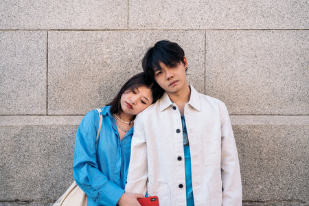 Young asian couple standing against gray wall posing and looking at camera.の写真素材