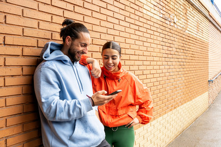 Young friends wearing sports clothes using mobile phone after working out. They are smiling and...