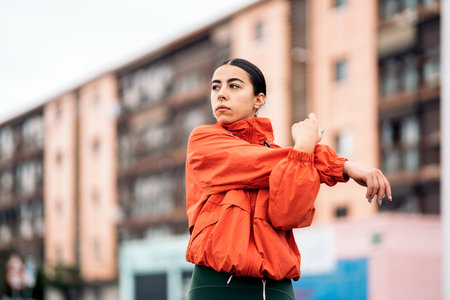 Young active woman wearing sports clothes looking at front and stretching after running in the city...