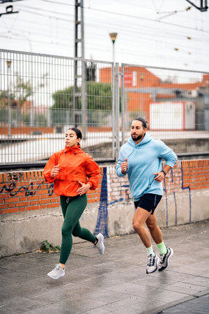 Active friends wearing sports clothes running in the city during rainy day. They are concentrated...