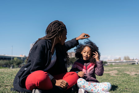 Happy black mother enjoying sunny day in the park with her adorable young daughter.の写真素材