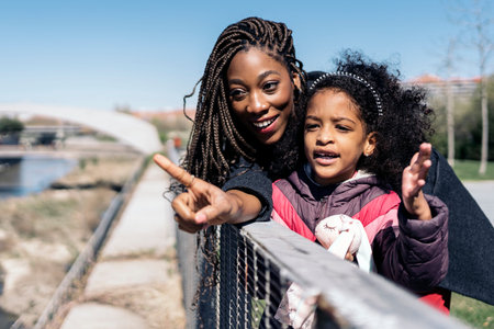 African woman spending sunny spring day in the park with her young daughter. They are looking at the...