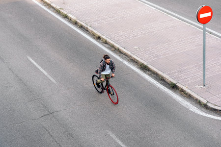 Handsome hipster man with long hair looking at front and riding his bike on the road.の写真素材