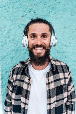 Cheerful man with long hair and big beard smiling and looking at camera against blue background. He...