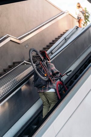 Unrecognized hipster man carrying his bike while walking up the escalators of the subway.の写真素材
