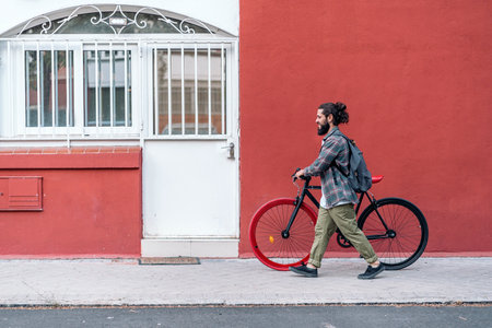 Bearded man walking with his cool bike in the street against red background.の写真素材
