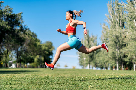 Strong asian woman with sports clothes working out in the park during sunny day. She is jumping in...