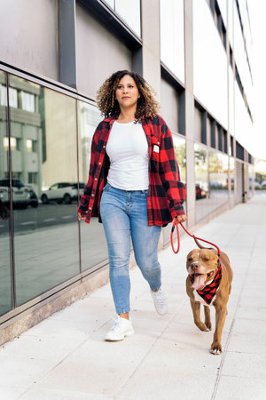 Happy black woman with curly hair walking her dog in the street and having fun.