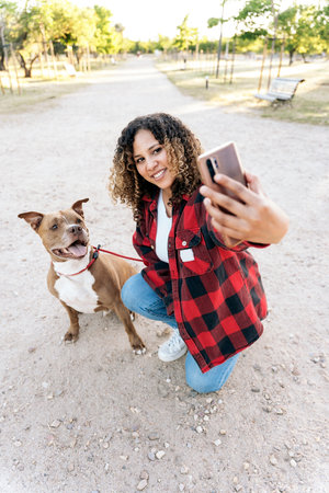 Happy woman with curly hair posing with her purebred dog and taking a selfie in the park.の写真素材