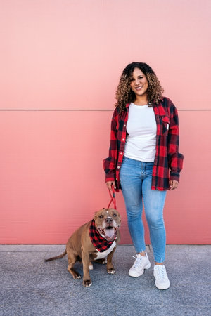 Cheerful african woman with curly hair standing in the street next to her adorable dog.の写真素材