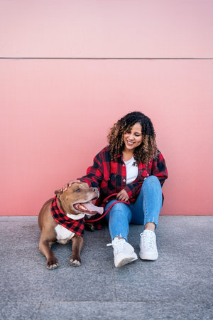 Cheerful african woman with curly hair sitting in the street next to her adorable dog.の写真素材