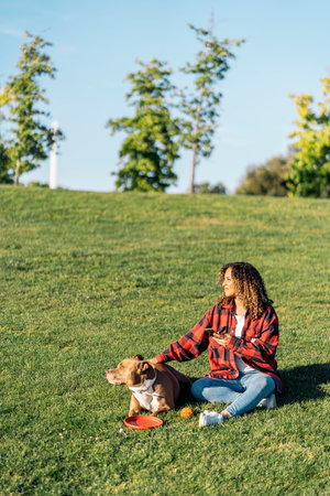 African woman sitting in the park with her dog and using her mobile phone.の写真素材