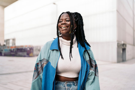 Happy and young african woman with cool braids smiling and looking at camera. She is in the street.の写真素材