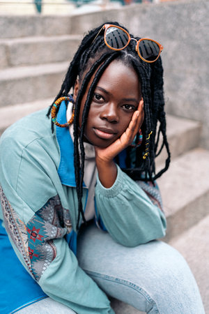 Expressive young african woman looking at camera outdoors and posing. She is sitting on stairs in the city.の写真素材