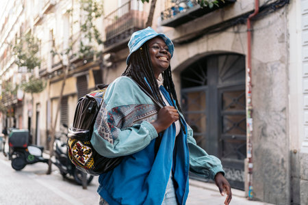 Happy and young african woman with cool braids smiling and walking in the city.の写真素材