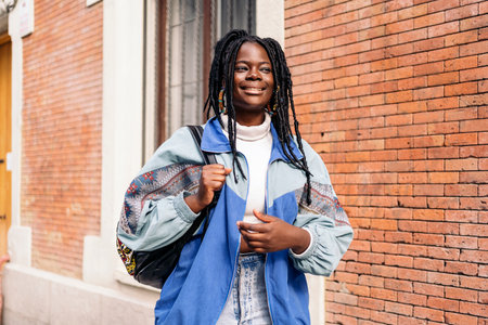 Cheerful african young woman with cool braids smiling and looking at front in the street.の写真素材