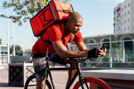 African american delivery man using his phone in the street and taking a break.