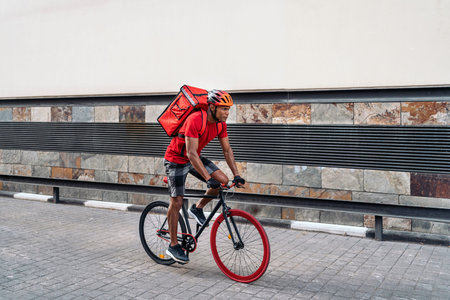 Focused delivery man carrying a package and using a safety helmet crossing the city with his bike.の写真素材