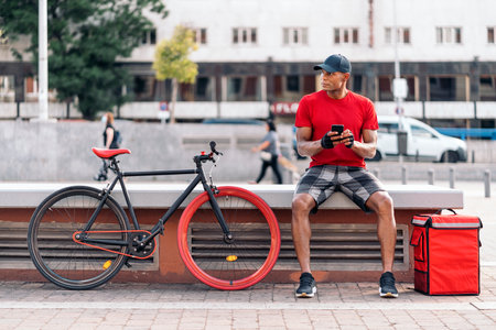 African messenger man sitting in the street using his phone and taking a break in his way to deliver a package.の写真素材