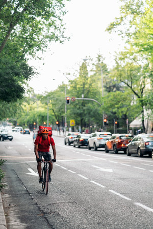 African delivery man wearing safety helmet riding his bike in the city on his way to deliver a package.の写真素材
